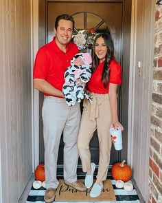 a man and woman standing in front of a door holding a baby wearing a cow costume