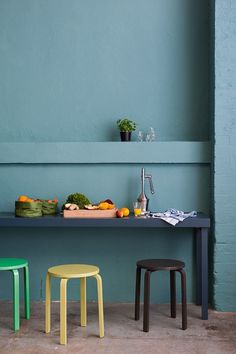 three stools in front of a table with fruit and vegetables on it, against a blue wall