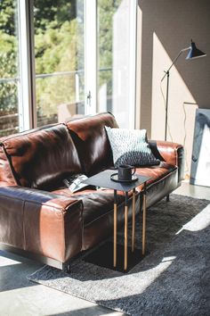 a brown leather couch sitting on top of a rug next to a table with a lamp