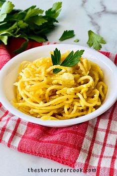 a white bowl filled with pasta and garnished with parsley on a red checkered towel