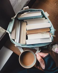 a person holding a cup of coffee next to a pile of books on a table