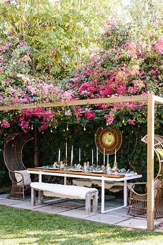 an outdoor dining area with wicker furniture and pink flowers on the wall behind it