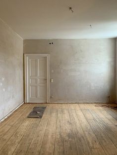 an empty room with hard wood flooring and white door on the wall behind it