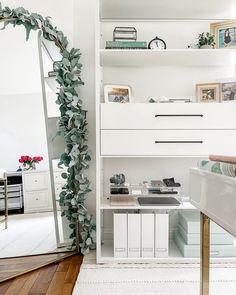 a living room with white furniture and green plants on the shelves, along with a mirror