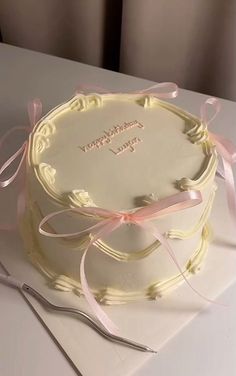 a white cake with pink ribbon on it and a fork sitting next to the cake