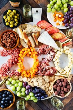 an assortment of cheeses, meats and fruit on a platter with wine glasses