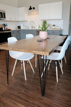 a wooden table with white chairs and a potted plant on it in a kitchen