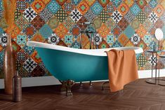 a bath tub sitting on top of a wooden floor next to a wall covered in colorful tiles