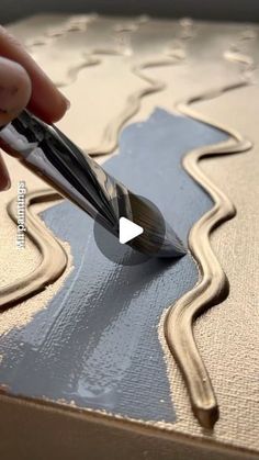 a person is using a pen to paint a piece of art with metallic foil on it