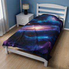 a bed in a room with blue walls and wooden floors is covered by a colorful galaxy comforter