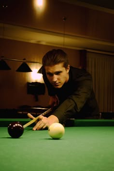 a man leaning over to hit a pool ball with his racket in a dimly lit room