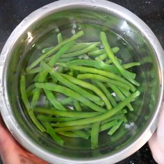 someone is holding a bowl with green beans in it