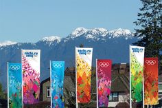 the olympic flags are lined up in front of some houses with mountains in the background