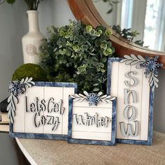 three wooden signs sitting on top of a table next to a potted green plant