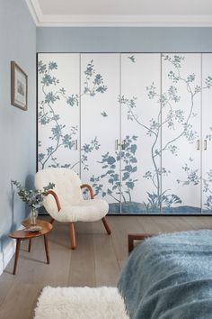 a bedroom with blue and white wallpaper, a chair and rugs on the floor