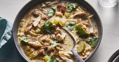 a bowl of chicken and vegetable soup with a spoon on the table next to it