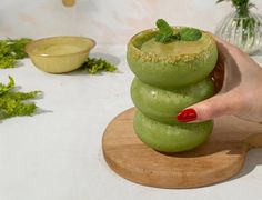 a woman is holding a green drink in her hand while standing on a wooden board