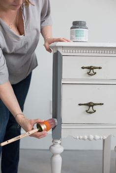 a woman is painting an old white table with paintbrushes and a spray bottle