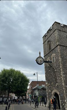 an old brick building with a clock on the side and people walking down the street