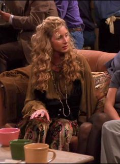 a woman sitting on top of a brown couch next to two cups and a table