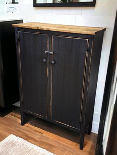 a black cabinet sitting on top of a hard wood floor next to a white sink