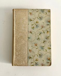 an old book sitting on top of a white wall next to a flowered cover