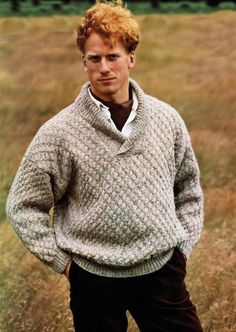 a man standing in a field wearing a sweater