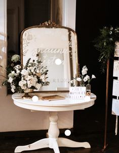 a white table topped with flowers and a mirror on top of it's stand