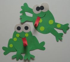 two green paper frogs with googly eyes on their faces, one is sticking its tongue out