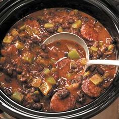 a crock pot filled with chili and sausages on top of a wooden table