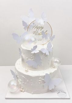 a three tiered cake with white butterflies on it and a happy birthday card in the middle