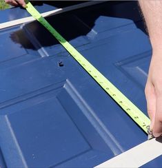 a person measuring the width of a blue door with a green tape on it's side