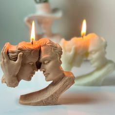 two candles that have been placed next to each other on a table with statues in the background