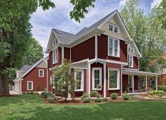 a red house with white trim on the front and side windows is surrounded by green grass