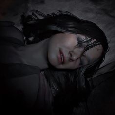 a woman is laying down with her eyes closed in the dark and she has long black hair