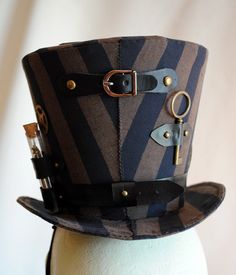 Steampunk all the way! This striking lady's top hat is covered with black and brown stripped fabric. It's main feature is a pair of metal silver toned goggles that sit at the center front...but that's only the beginning! Numerous gears are strategically placed here and there along with two long vials filled with watch parts and an antique bronze key at the back. The whole piece wouldn't be complete without a series of black leatherette straps and antique bronze studs pump up the steam! Measureme Black Steampunk Top Hat For Alternative Fashion, Fitted Black Steampunk Top Hat, Black Fitted Steampunk Top Hat, Brown Leather Steampunk Top Hat, Top Hats For Women, Steampunk Top, Steampunk 4" Top Hat, Steampunk Top Hat, Man Hat