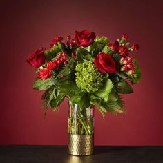 a vase filled with red roses and greenery