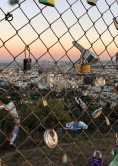 the view from behind a chain link fence with many objects hanging on it and buildings in the background