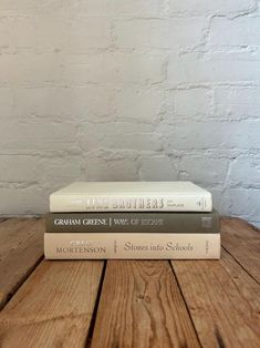 two books sitting side by side on top of a wooden table next to a white brick wall