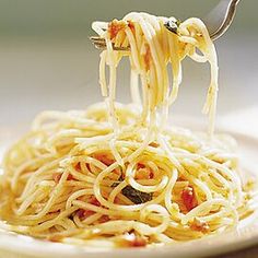 someone is eating spaghetti from a white plate with a fork in their hand and the noodles are being held up