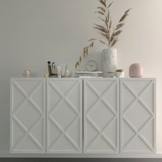 a white sideboard with various items on it and a plant in the corner next to it