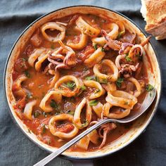 a bowl filled with pasta and meat on top of a blue cloth next to bread