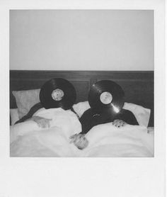 black and white photograph of two people laying in bed with vinyl records on their heads