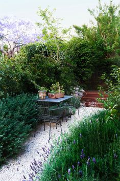 an outdoor table and chairs in the middle of a garden with purple flowers on it