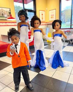 a young boy in an orange blazer and blue skirt standing next to other dolls