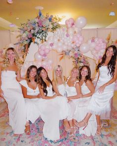 a group of women in white dresses posing for a photo with balloons and streamers