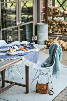 a table with food and wine glasses on it next to some wood stacked in the background