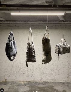 three bags hanging from hooks in an empty room with cement walls and concrete flooring