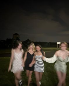 four women in short dresses are posing for a photo on the grass with their arms around each other