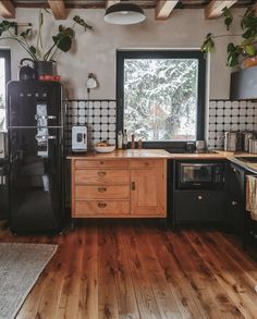 a kitchen with wooden floors and black appliances in the center, surrounded by potted plants